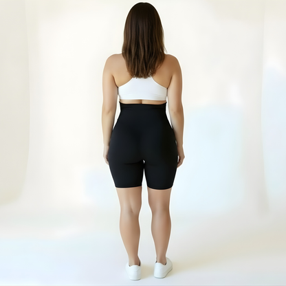 Back view of a woman wearing high-waisted black compression shorts and a white sports bra, highlighting coverage, comfort, and seamless structure — KORFORM activewear.