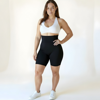 Woman wearing high-waisted black compression shorts and a white sports bra on a soft beige background — Scandinavian minimalist style by KORFORM.