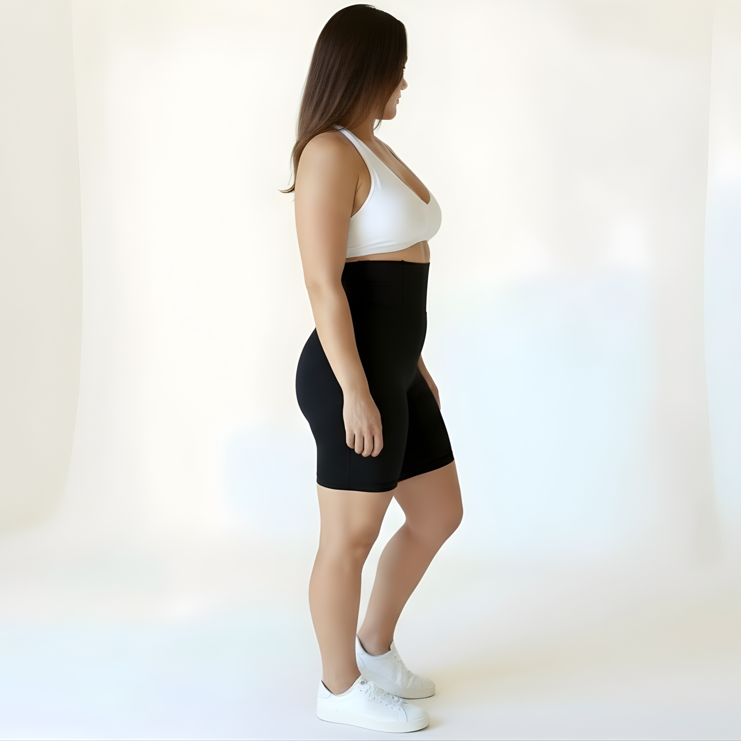 Side view of a woman wearing high-waisted black compression shorts and a white sports bra, showing the supportive waistband and smooth matte finish — KORFORM Scandinavian design.