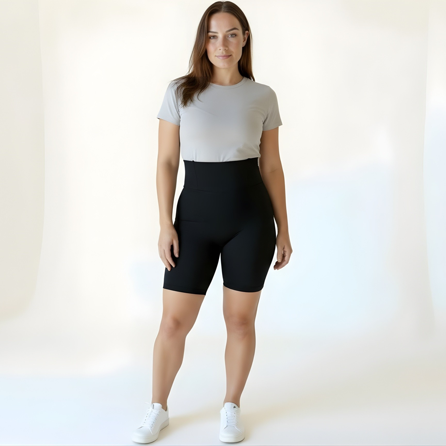 Woman wearing high-waisted black compression shorts and a grey gym t-shirt, standing front-on with both feet flat on the ground, showing everyday versatility — KORFORM activewear.